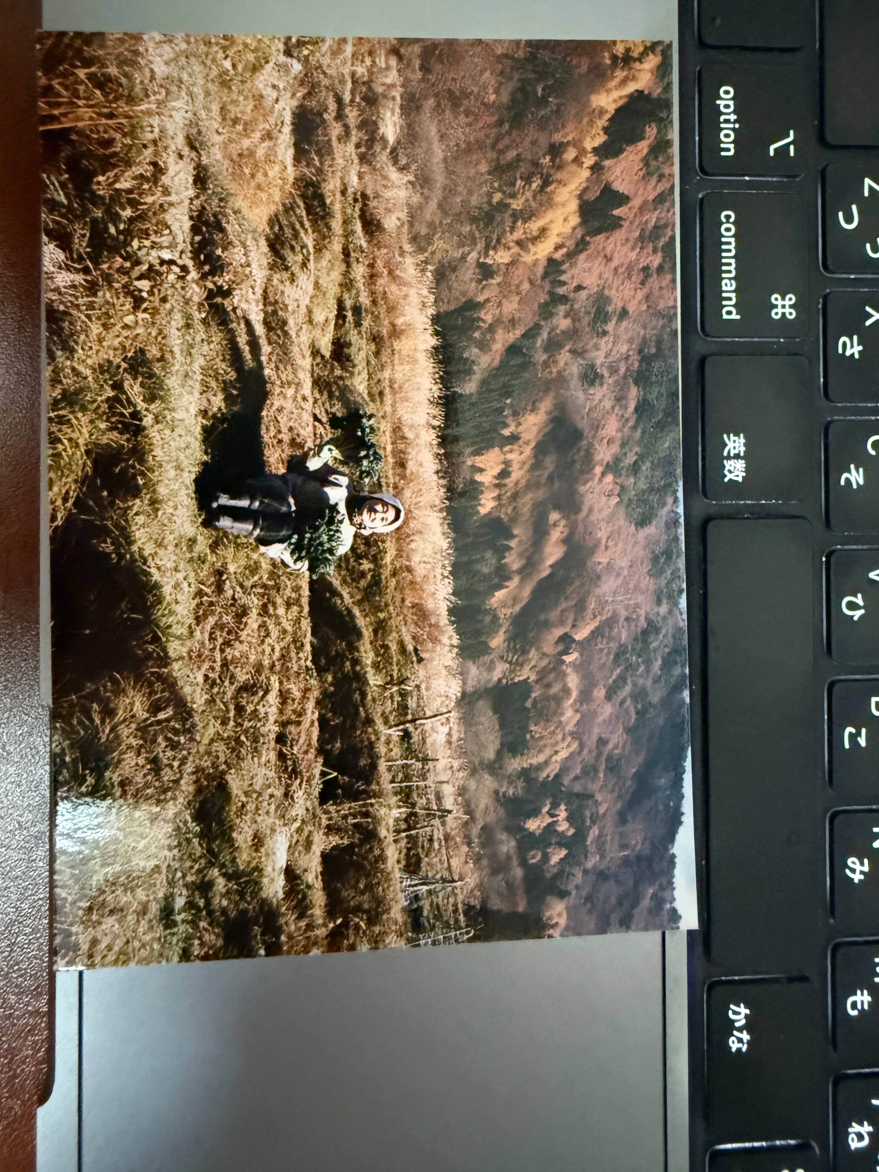 秋の山を背景に、畑で野菜を抱える母の古い写真